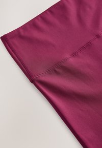 Maroonfarbenes Sportgewebe mit glatter Textur, versehen mit Flatlocknähten und einer eng anliegenden Passform. Geeignet für Sportbekleidung.