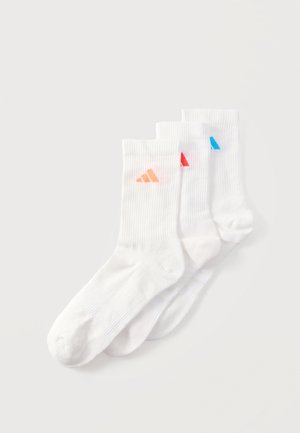 Kolm paari valgeid soonikkoes kootud poolpikka sokke, mille pahkluuosas on väikesed oranži, punase ja sinise toonis Adidas logod, virnas valgel taustal.