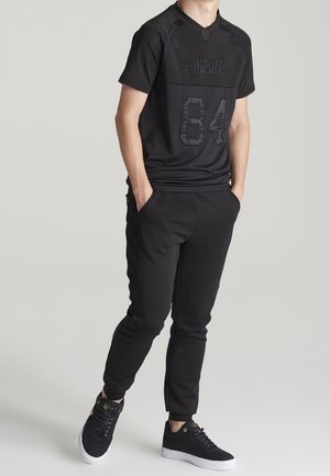 Conjunto atlético negro que incluye una camiseta de manga corta con números y logotipo en relieve, combinada con pantalones ajustados y zapatillas negras.