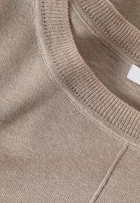 Beige kötött pulóver kerek nyakkivágással. A texturált anyag finom szövésű, enyhén bordázott széllel, ami hangsúlyozza a puhaságát.