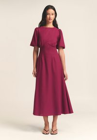 Burgundin, polvipituinen mekko, jossa on lyhyet puffihihat, muotoiltu yläosa ja valuva hame; valmistettu kevyestä kankaasta.