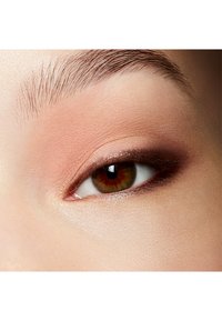 Närbild på ett öga med mjuk persikoögonskugga på ögonlocket, ljusbrun iris och naturligt ögonbrynshår, vilket visar på en jämn hudstruktur.