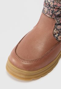 Bota de couro castanho claro com sola de borracha grossa e forro de tecido floral visível no tornozelo.