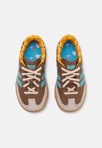 Brown and beige sneakers with blue stripes, textured leather, and a patterned yellow lining. Features rounded toe and beige rubber sole.