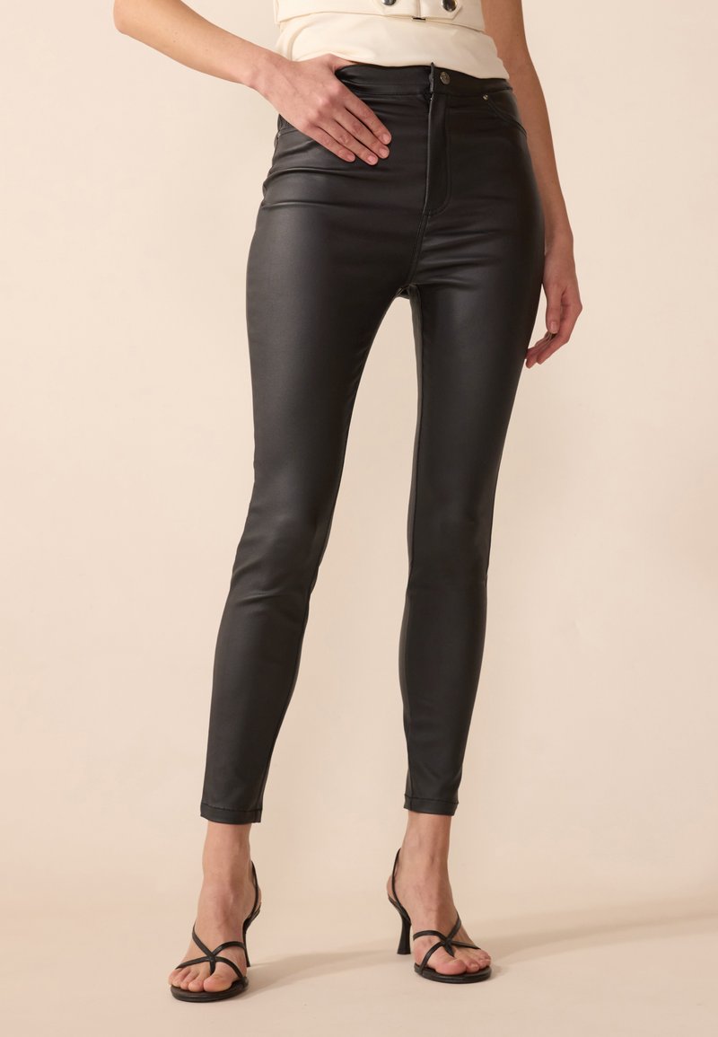 High-waisted black faux leather leggings with a fitted silhouette, smooth texture, and stitch detailing along the seams.