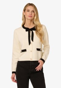 Cremfarbener Cardigan mit schwarzem Besatz, Rundhalsausschnitt und Schleife. Verfügt über zwei schwarze Taschen mit dekorativen Knöpfen und langen Ärmeln.