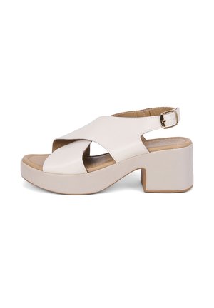 Sandale beige en cuir à bout ouvert avec larges brides croisées, talon bloc, semelle coussinée et bride de cheville réglable avec boucle.