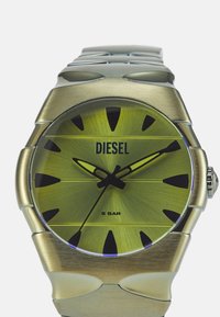 Orologio Diesel con quadrante metallico verde, audaci indici delle ore neri, cassa in tono argento e un ampio bracciale in acciaio inossidabile. Resistente all'acqua fino a 5 bar.