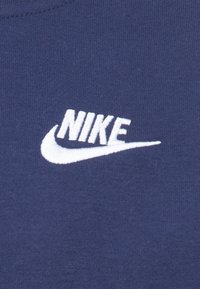 O tecido azul marinho apresenta um proeminente logótipo "Nike" bordado em branco com um swoosh, exibindo uma textura suave e uma marcação clara.