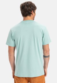 Mátově zelené bavlněné tričko s krátkým rukávem a kulatým výstřihem, s hladkou texturou, z pohledu zezadu. Bez viditelných vzorů nebo grafiky.
