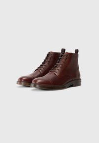 Bruine leren enkelboots met een gestructureerde afwerking, vetersluiting, ronde neus en subtiele contrasterende stiksels op de bovenkant.