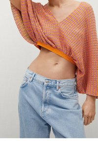 Top en crochet rose et orange avec un décolleté en V, des manches amples et une taille froncée. Associé à un jean taille haute bleu clair.