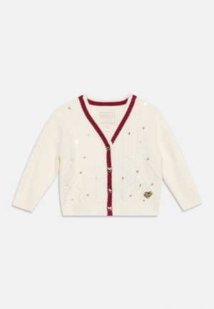 Cardigan blanc à maille torsadée avec bordure rouge, boutons en forme de cœur, petits accents de sequins et un emblème cœur doré sur le bas.