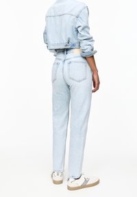 Veste en denim bleu clair raccourcie avec manches retroussées et deux poches arrière, associée à un jean bleu clair fuselé. Des baskets blanches complètent la tenue.