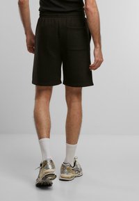Shorts en coton noir avec une coupe décontractée, taille élastique et une poche arrière unique. Portés avec des chaussettes blanches et des baskets aux accents argentés.