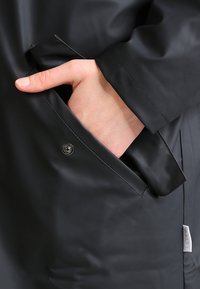 Czarna wodoodporna kurtka z boczną kieszenią zapinaną na zatrzask, gładką teksturą oraz nowoczesnym designem z minimalistycznymi akcentami.