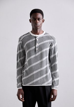 Cămașă cu mâneci lungi alb-negru, cu o textură ribbed, având un guler cu nasturi și un model geometric format din linii verticale și diagonale.
