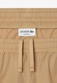 Pantalones cortos de corte relajado de Lacoste en beige, con una cintura elástica texturizada, que incluye un cordón ajustable y una etiqueta de marca en la parte delantera.