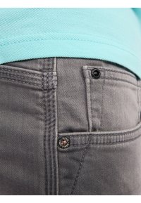 Jeans grises con una tela texturizada, que presentan un pequeño bolsillo frontal con un botón negro. Arriba, una camisa de color azul claro con un cuello acanalado.