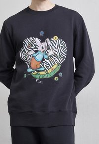 Felpa di cotone nera con una grafica colorata di un cartone animato che raffigura un coniglio su un baccello verde, contro uno sfondo a cuore con strisce zebrate.