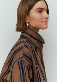 Braun gestreifte Knopfjacke mit blauen Linien. Verfügt über einen hohen Kragen und strukturierte Stoffqualität. Enganliegender Stil mit sichtbaren Nähdetails.