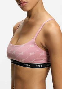 Roze beha met wit "Hugo" logo patroon, voorzien van een zwarte elastische band aan de onderkant. Verstelbare roze bandjes en een gladde stoftextuur.