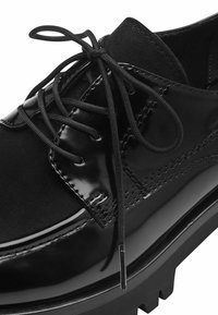 Schwarze Lacklederschuhe mit Wildlederakzenten, runde Zehenform und schwarzen Schnürsenkeln. Merkmale sind die dicke, strukturierte Sohle mit Zickzackmuster.
