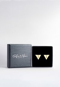 Orecchini triangolari in oro con accenti di gemme trasparenti, esposti in una scatola di gioielli nera e testurizzata con un logo sul davanti.