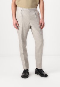 Ljusgrå skräddarsydda byxor med ett strukturerat mönster, veckad front och slim fit, kombinerade med svarta läderskor.