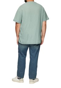 Korte mouwen, ronde hals T-shirt in lichtgroene stof, met een relaxte pasvorm, gecombineerd met donkerblauwe straight-leg jeans en witte sneakers.