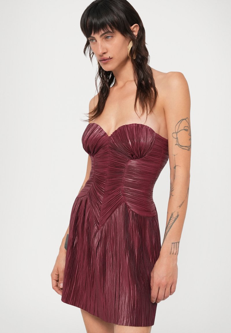 Strapless bordeaux mini-jurk met geplooide textuur, aansluitende bovenkant en uitlopende rok. Beschikt over een gestructureerd ontwerp met een geometrisch naadpatroon.