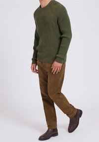 Grüner gerippter Strickpullover, braune Cordhosen und braune Chelsea-Stiefel. Der Pullover hat einen Rundhalsausschnitt, eine strukturierte Oberfläche und lange Ärmel.
