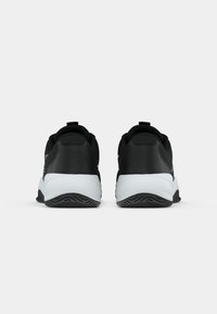 Chaussures de sport noires avec une tige lisse, une semelle intermédiaire blanche, un talon texturé et une forme arrondie. Présentent un marquage minimal et une languette arrière.