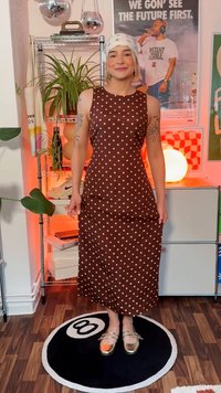 Vestido maxi de lunares marrones con un cuerpo ajustado y falda acampanada. Presenta un escote redondo y una tela suave. Combinado con zapatos metálicos dorados.