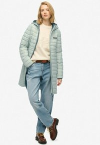 Lys blå, polstret lang frakke med hætte, lynlås lukning og kviltet tekstur. Båret over en cremefarvet sweater og lyseblå jeans, parret med brune støvler.