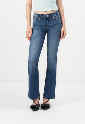 Blå denim flared jeans med en lett falming, femlommers design, beltestropper og en tettsittende midje. Brukt med svarte spisse hæler.