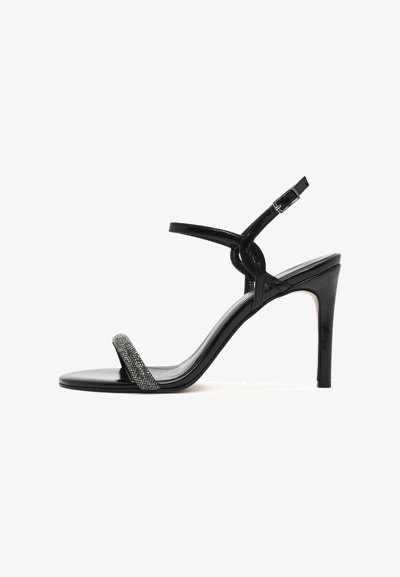Sandale noire à talons hauts avec une finition en vernis lisse, dotée d'une fine lanière ornée de décorations en métal argenté et d'une boucle à la cheville.
