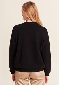 Maglione nero a maglia con vestibilità comoda, polsini e orlo a coste. Presenta un motivo texturizzato e un classico scollo tondo.