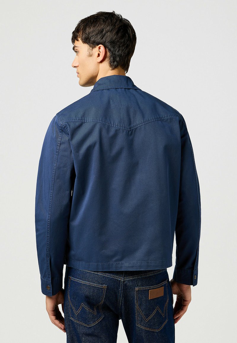 Granatowa bawełniana koszula z kołnierzykiem, długimi rękawami i mankietami zapinanymi na guziki. Gładka faktura i minimalistyczny design bez widocznych wzorów.