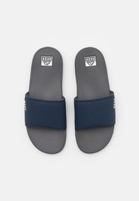 Infradito blu navy con una fascia texturizzata, suole in gomma e un morbido sotto-piede grigio. Presentano un logo sulla fascia e sul sotto-piede.