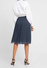 Gonna plissettata blu navy con un motivo sottile, realizzata in tessuto leggero. Abbinata a una blusa bianca e tacchi neri con cinturini.