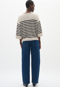 Top a righe, beige e nero, in maglia con maniche ampie, abbinato a jeans in denim blu a vita alta e dalla vestibilità morbida. Design semplice e colori neutri.