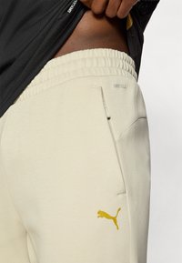 Ανοιχτά μπεζ φόρμες με ελαστική μέση, με τσέπη και κίτρινο  λογότυπο Puma. Κατασκευασμένες με υλικό DryCell για έλεγχο της υγρασίας.