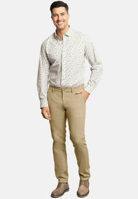 Camisa de botones con un fondo claro, decorada con pequeñas flores azules, combinada con unos pantalones beige de corte slim y zapatos marrones con cordones.