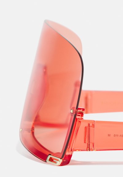 Gafas de sol rojas transparentes con un diseño de lente curvada y de gran tamaño. Presentan un armazón transparente y herrajes de bisagra con detalles en dorado.