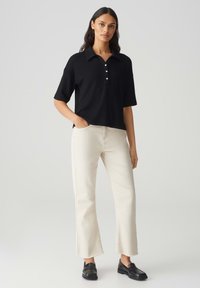 Polo noir à manches courtes avec col et patte de boutonnage à trois boutons ; associé à un jean droit écru et des mocassins noirs. Look propre et décontracté.