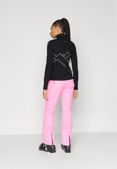 Črni pulover z dolgimi rokavi z gorniškim motivom na hrbtu, kombiniran z rožnatimi smučarskimi hlačami. Obleka ima oprijet kroj in kontrastne teksture.