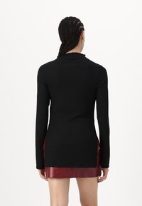 Black long-sleeve top with ribbed texture, featuring a mock neckline and side slits, worn over a burgundy leather mini skirt.