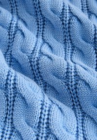 Gros plan sur un tissu tricoté bleu doux présentant des motifs de torsades tressées en relief en rangées verticales.