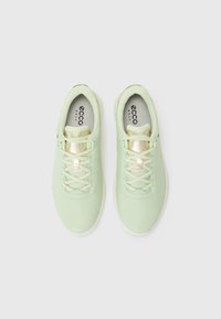 Tênis atléticos verde claro com uma textura suave, apresentando uma língua em malha, design com atacadores e um detalhe dourado na língua.